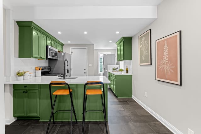 Kitchen with deep green cabinets, white countertops, and a peninsula with seating